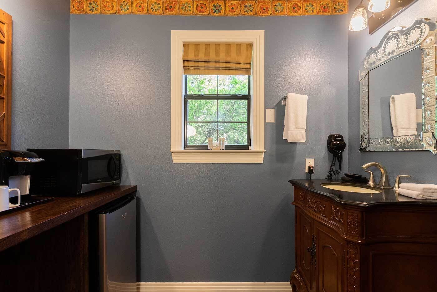 Une salle de bain avec une fenêtre, un lavabo, un miroir et un four à micro-ondes posé sur un comptoir.