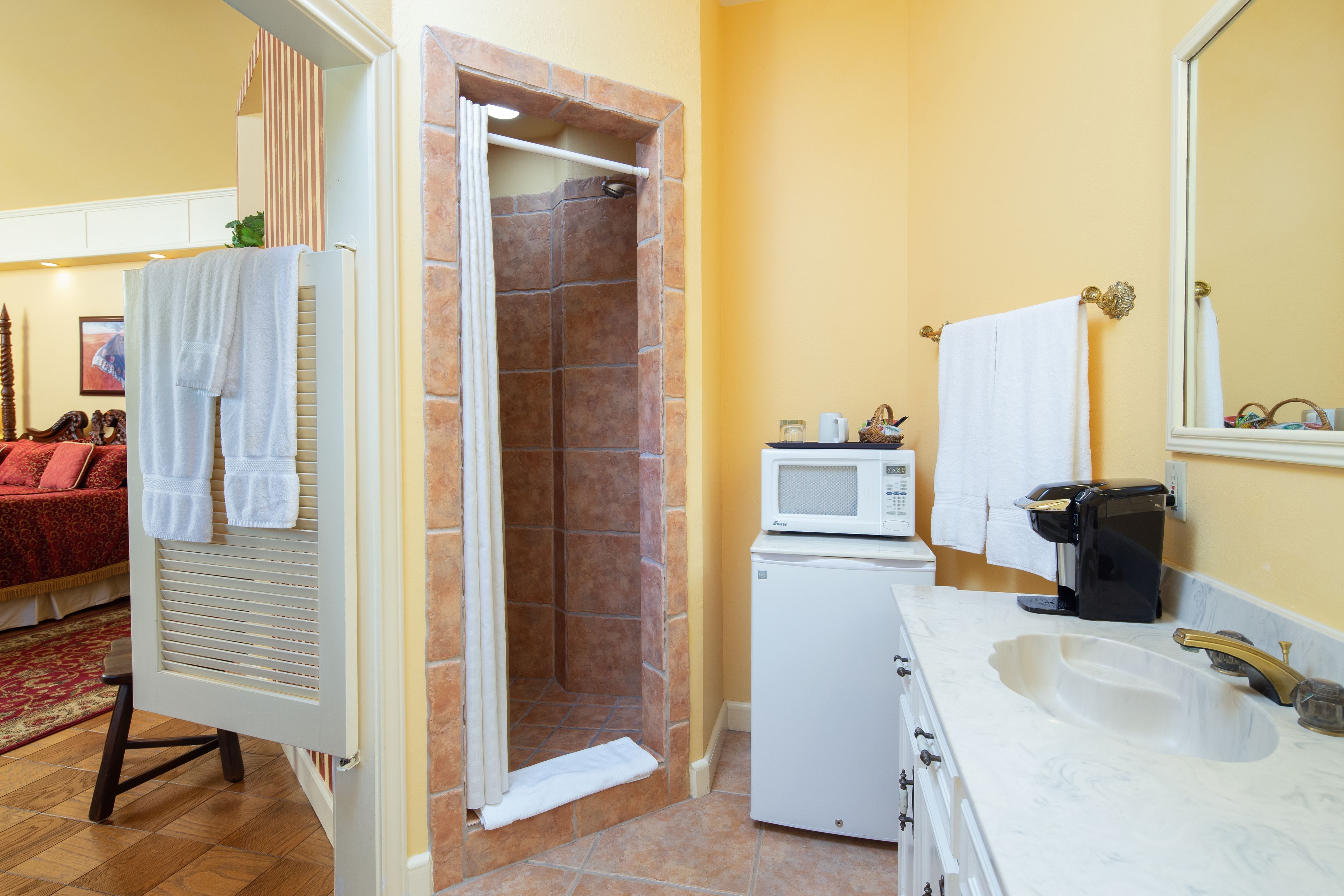 A bathroom with a shower, a microwave, a sink, and a coffee maker.