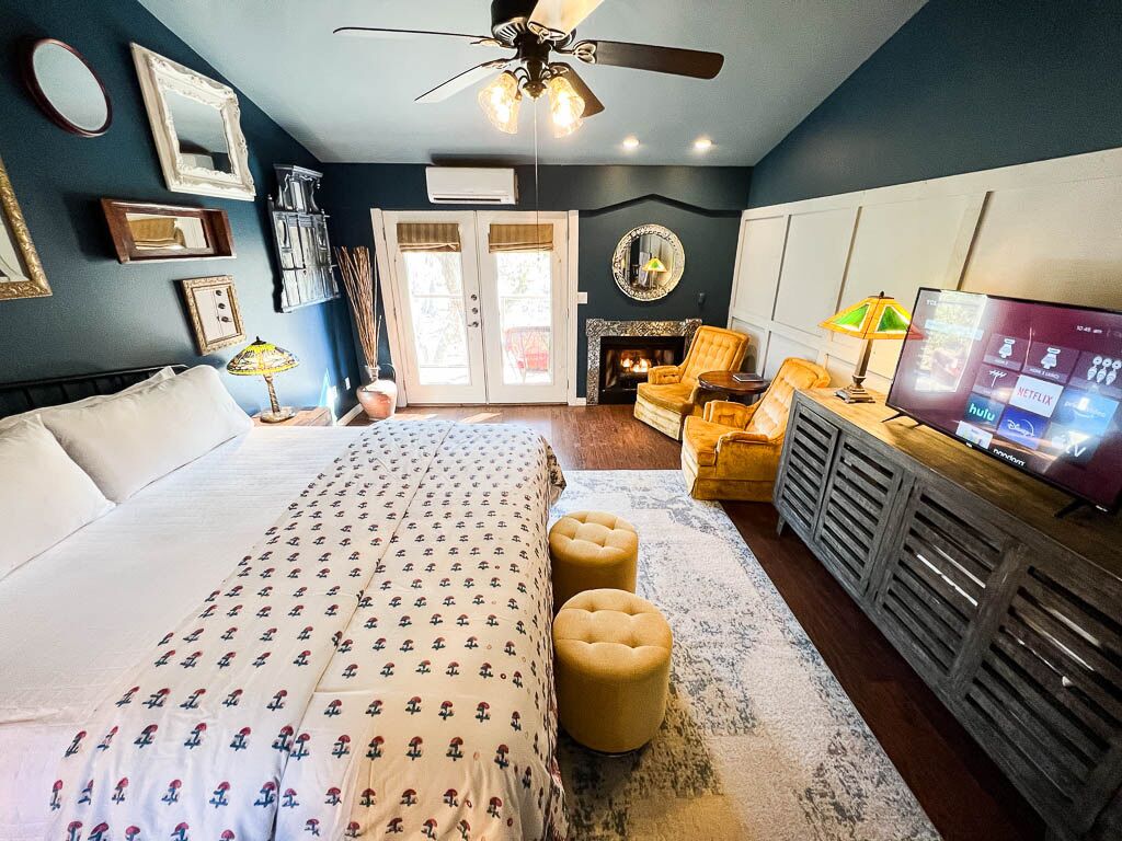 A bedroom with a bed, ottomans, a TV, and a fireplace.