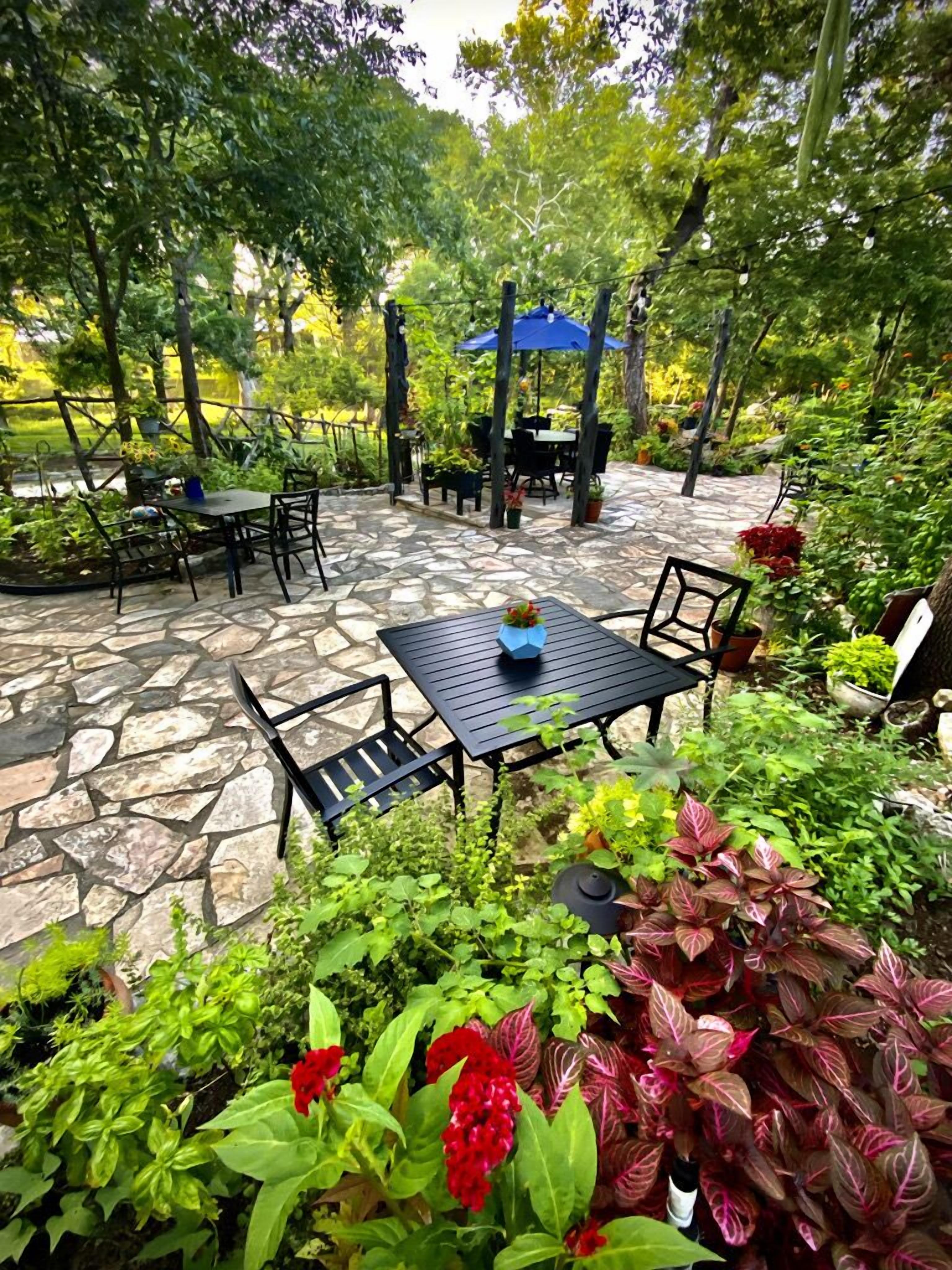 An outdoor patio area with stone flooring, tables, chairs, and a blue umbrella.