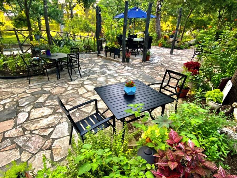 An outdoor patio area with stone flooring, tables, chairs, and a blue umbrella.