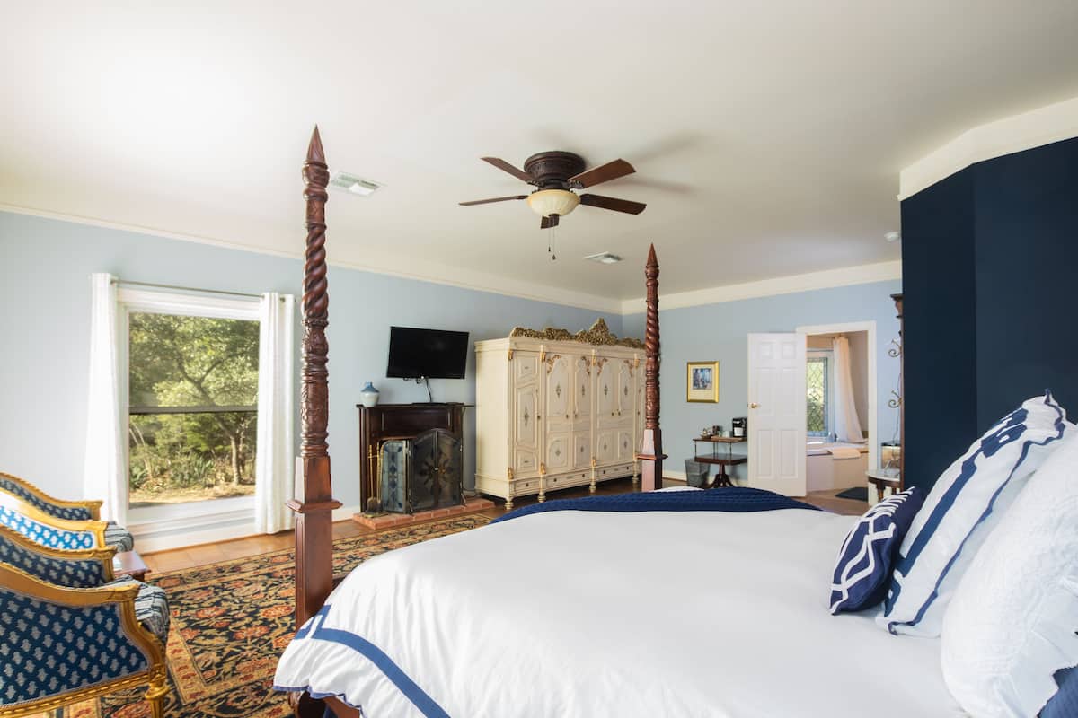 A spacious bedroom with a large bed, a ceiling fan, a wooden wardrobe, a television, and a view of the outdoors.