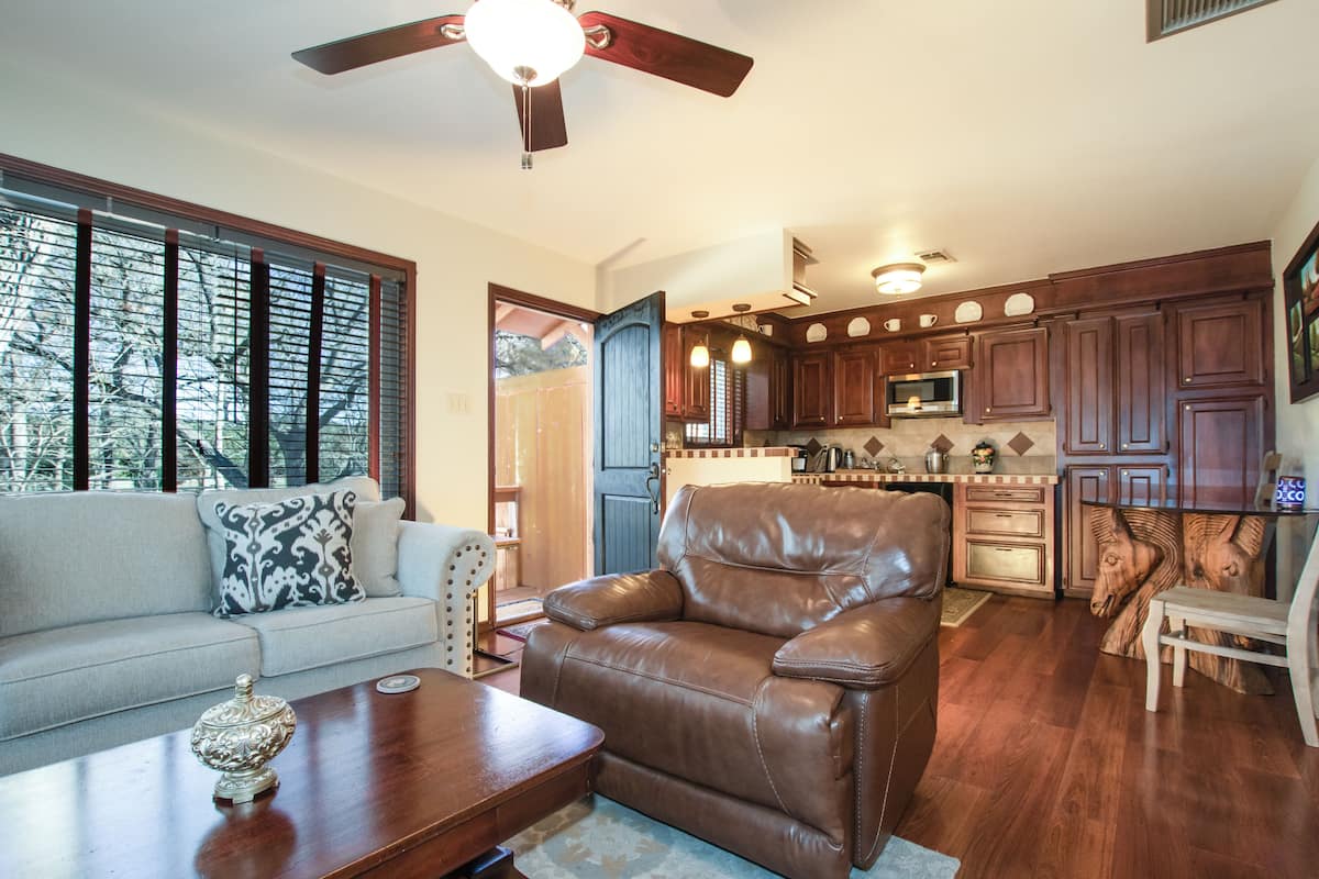 A spacious living room with a leather sofa, a wooden coffee table, and a ceiling fan.