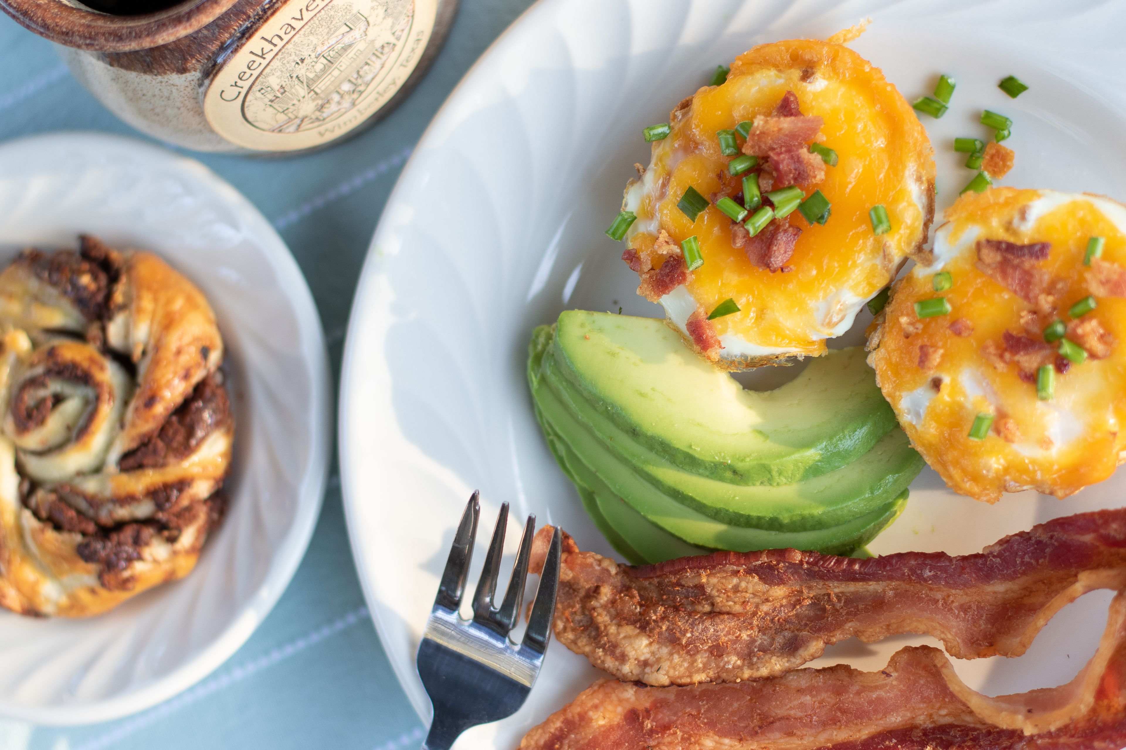 Un plato de desayuno con huevos, tocino, aguacate y un pastel.