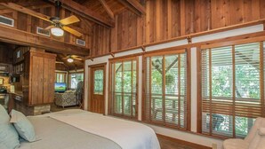 A wooden cabin interior with a large bed, a dining area, and a view through the windows. - Creekhaven Inn & Spa (Wimberley)
