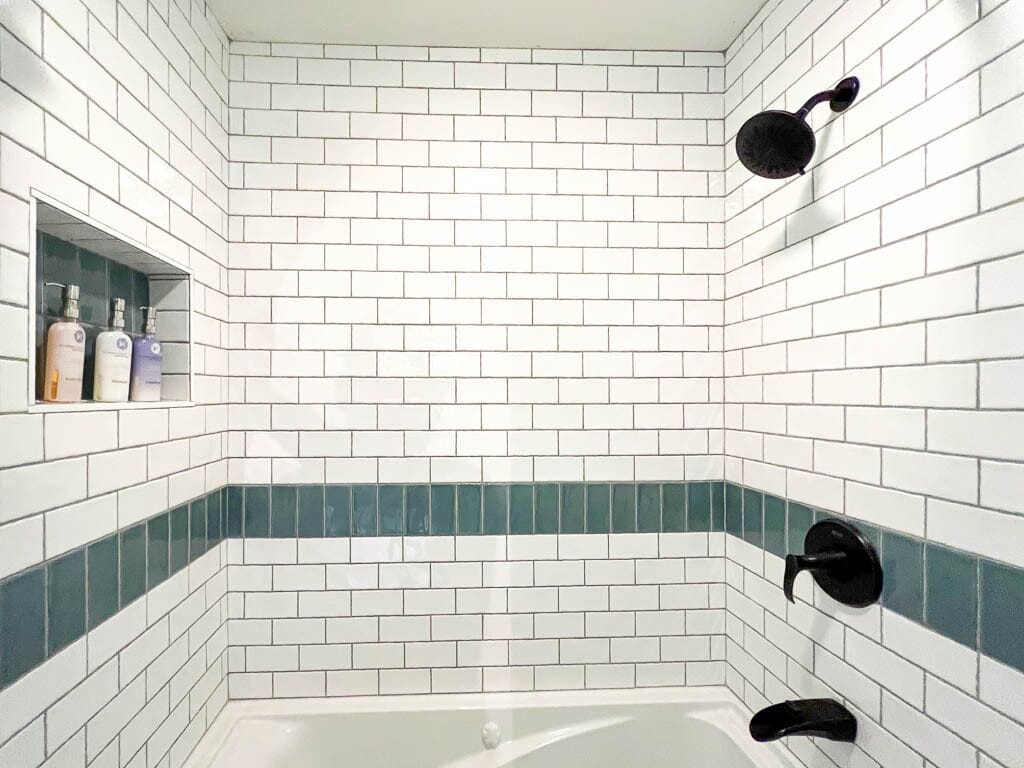 A bathroom with white subway tiles, a green accent border, and black towel hooks.