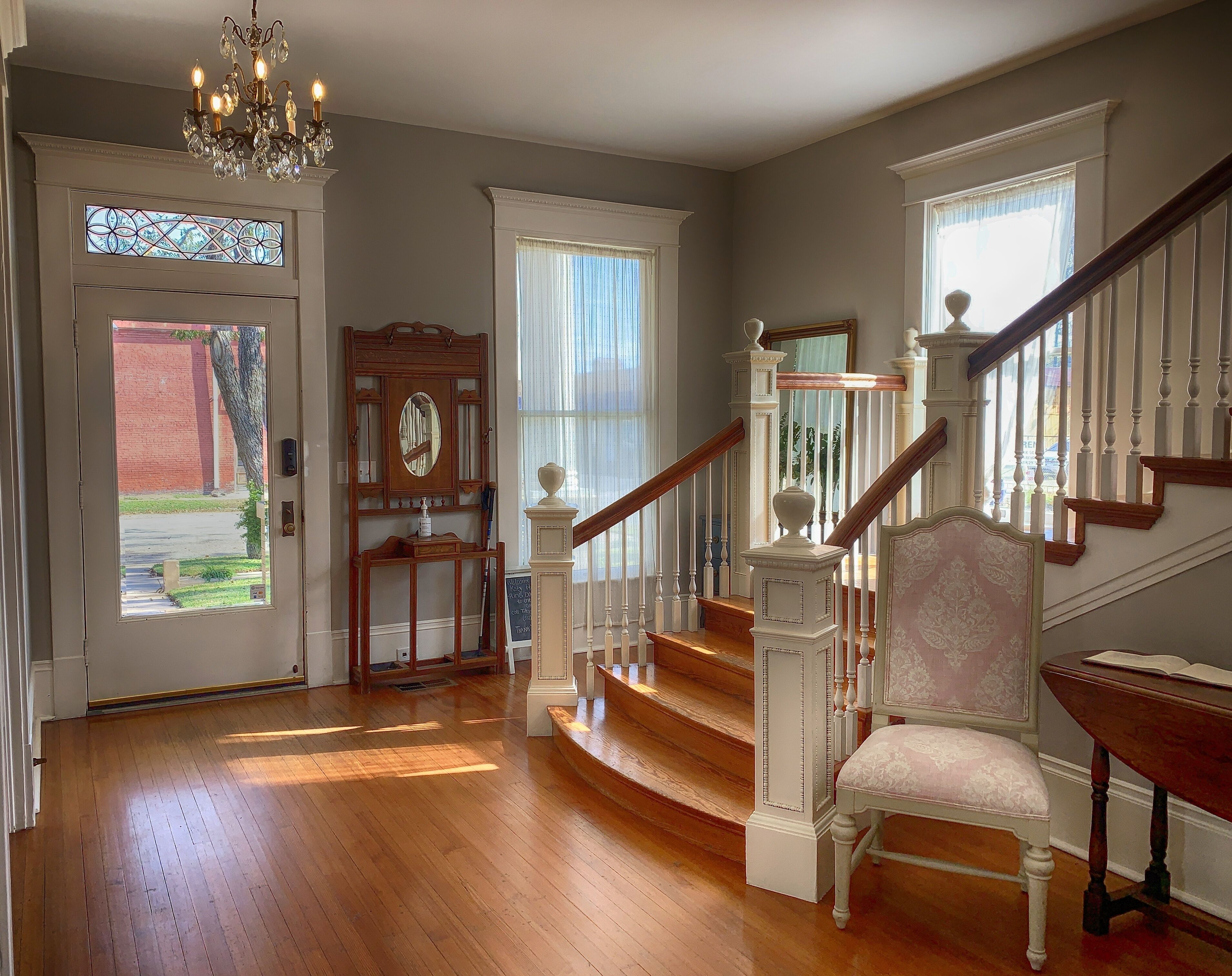 A grand entryway with a wooden staircase, a chandelier, and a chair.