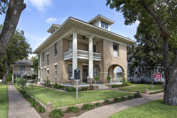 A two-story building with a central balcony, a covered front porch, and a brick facade.