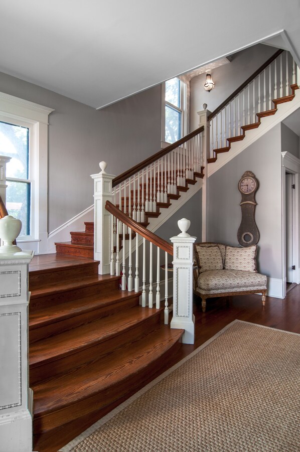 A staircase with wooden steps and white balusters, a patterned armchair, and a wall clock.