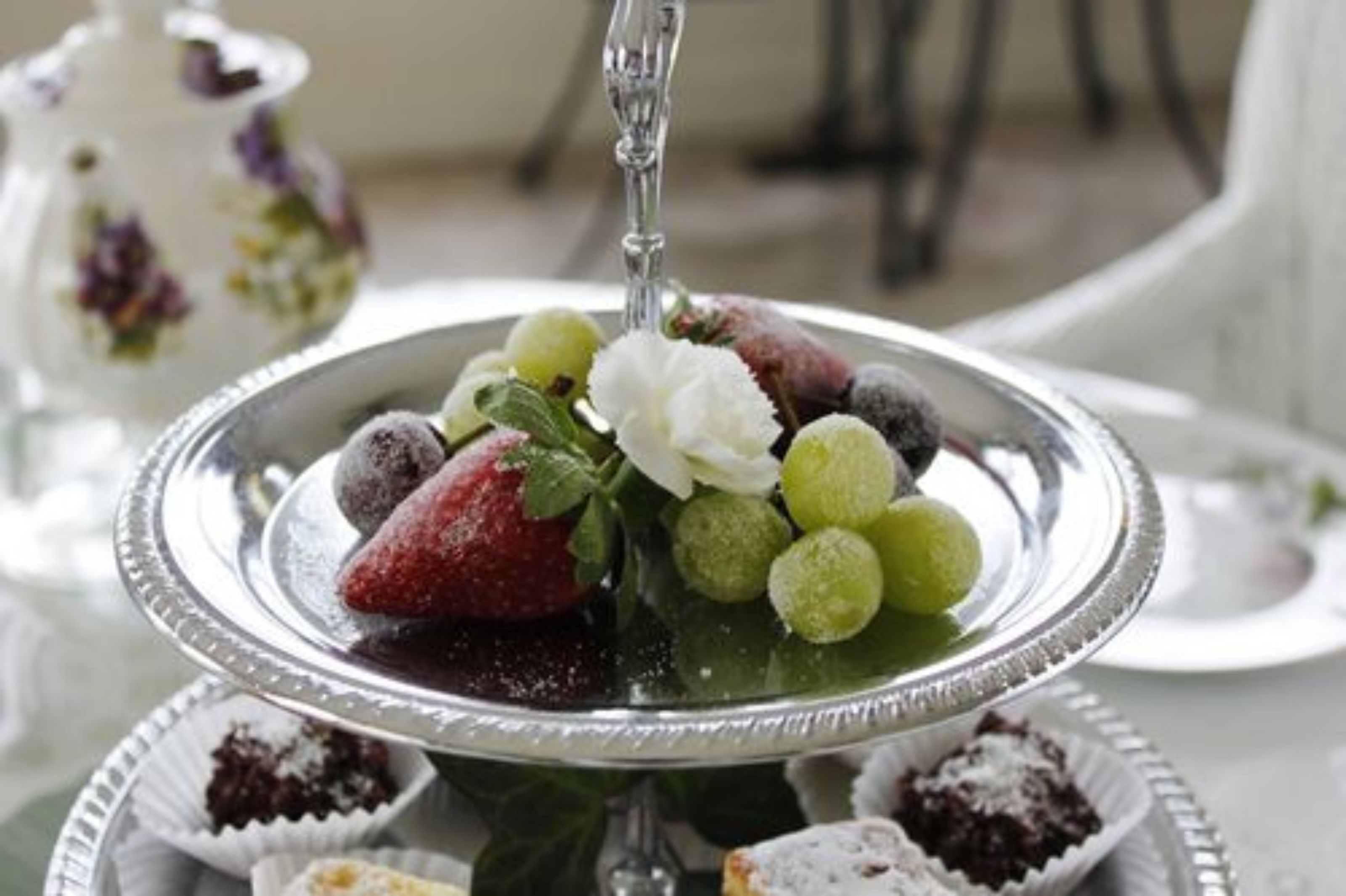 A silver dessert plate with strawberries, grapes, and a white flower, surrounded by smaller plates with desserts.