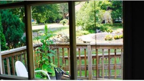 A view from a window with a wooden deck and greenery outside.