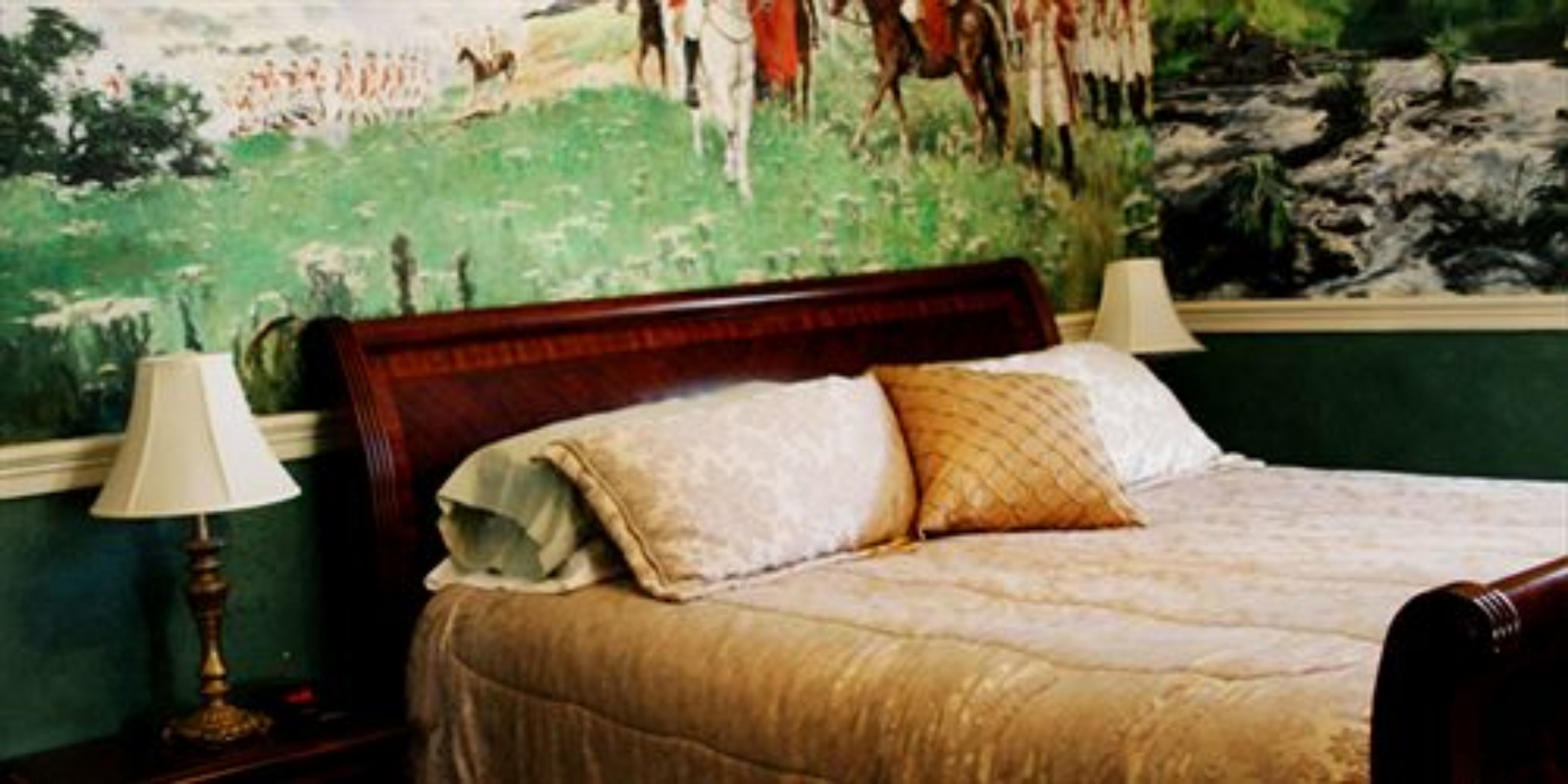 Un dormitorio con una cama de madera, dos lámparas de noche y un cuadro grande de una escena histórica en la pared.