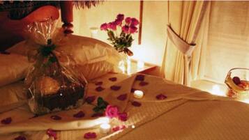 A bed with rose petals, a candle, and a basket of fruit.