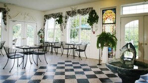 A room with a checkered floor, black and white chairs, a fountain, and a stained glass window.