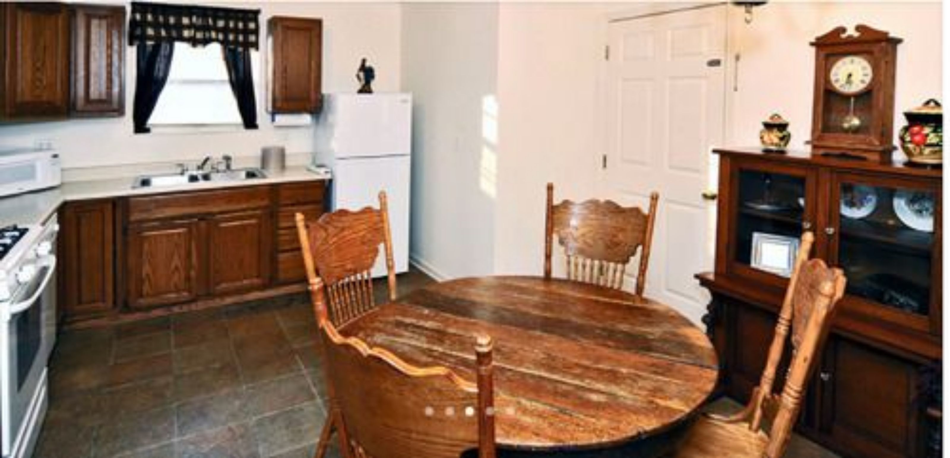 A kitchen with wooden cabinets, a white refrigerator, a round wooden dining table, and a clock on a wooden cabinet.