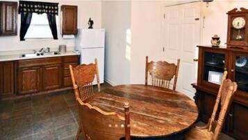 A kitchen with wooden cabinets, a white refrigerator, a round wooden dining table, and a clock on a wooden cabinet.