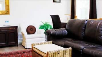 A living room with a brown leather sofa, a white armchair, a dark wooden cabinet, and a green plant.