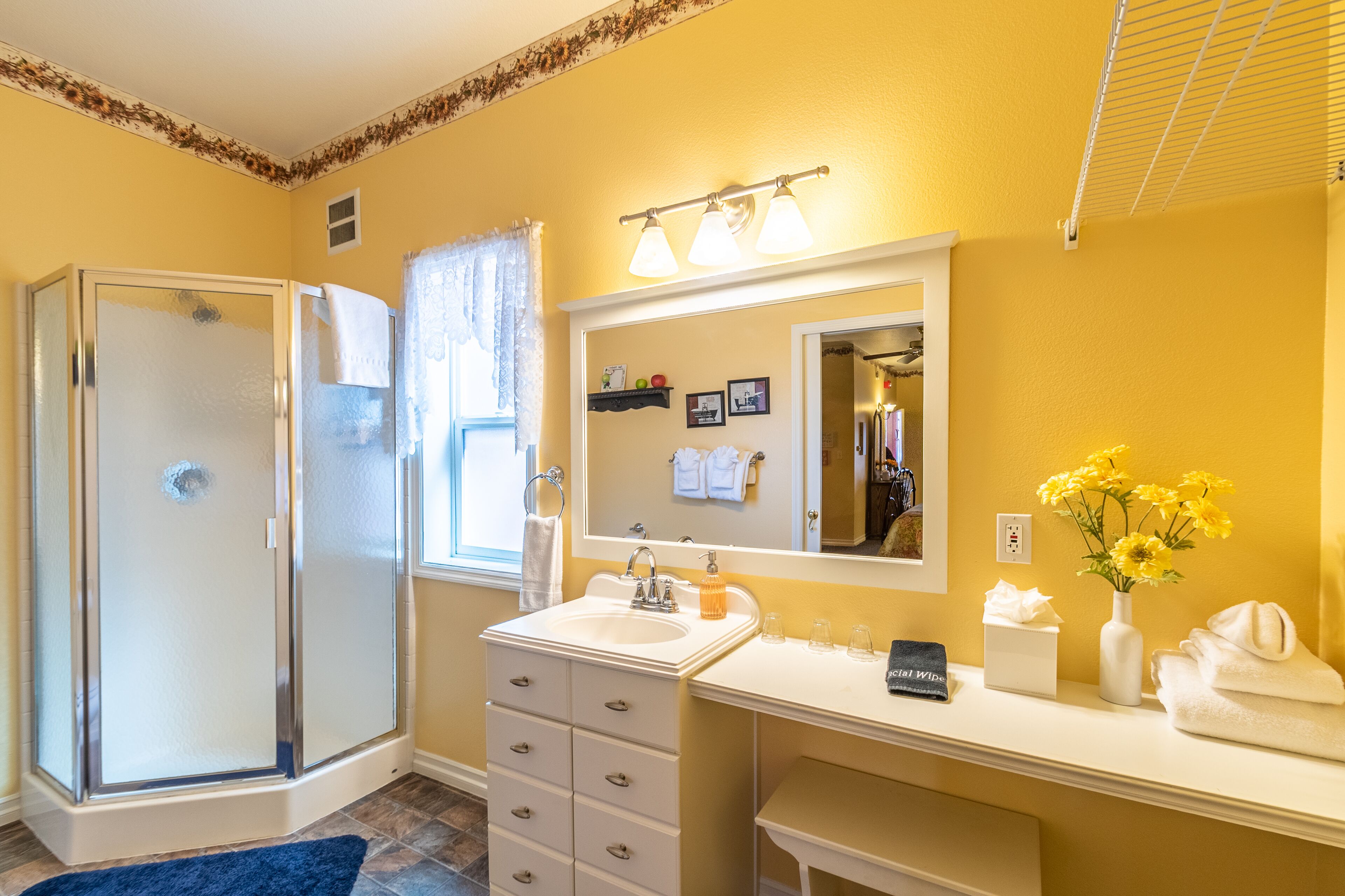 A bathroom with a glass shower enclosure, a sink with a mirror above it, and a vanity with a vase of flowers.