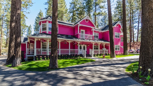 Una casa rosa con un portico, circondata da alberi.