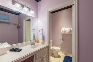 Een badkamer met een witte wastafel, spiegel en toilet. Handdoeken hangen aan de muur en er ligt een blauw vloerkleed op de vloer.