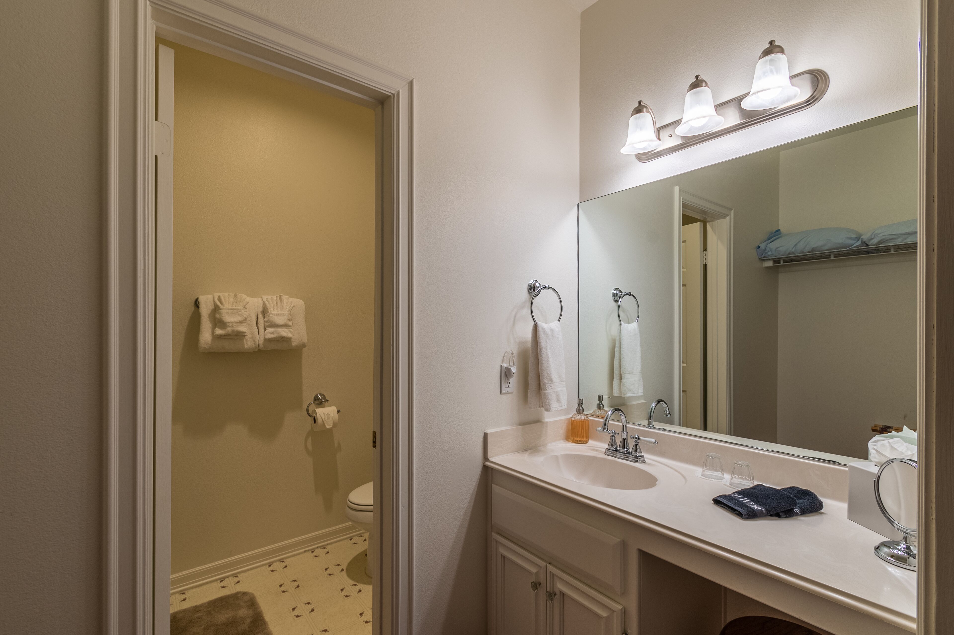 Un baño con lavabo blanco, espejo y toallero.