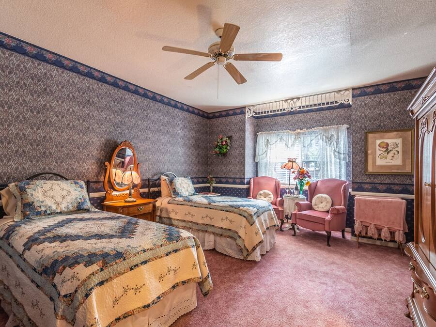 A bedroom with two beds, a ceiling fan, a dresser, a chair, and a window with curtains.