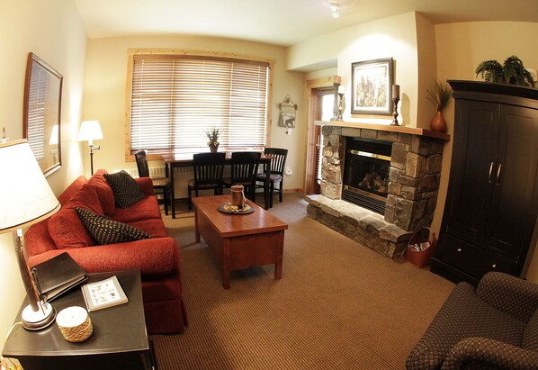 A living room with a fireplace, a sofa, a coffee table, and a dining area with chairs and a table.