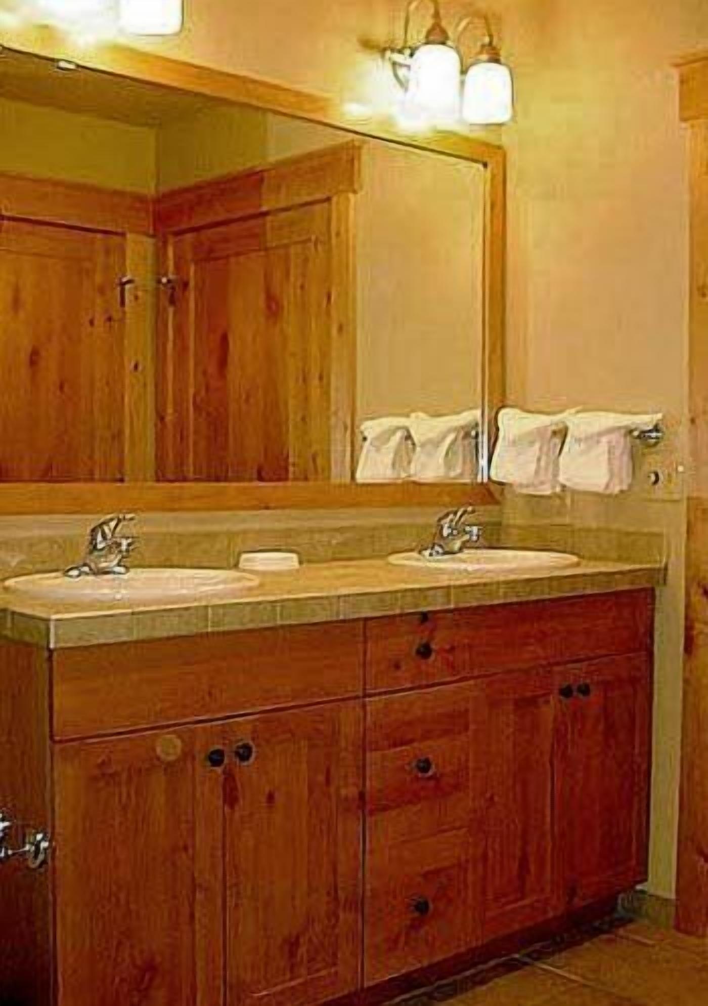 A wooden bathroom with a large mirror, two sinks, and a cabinet with drawers.