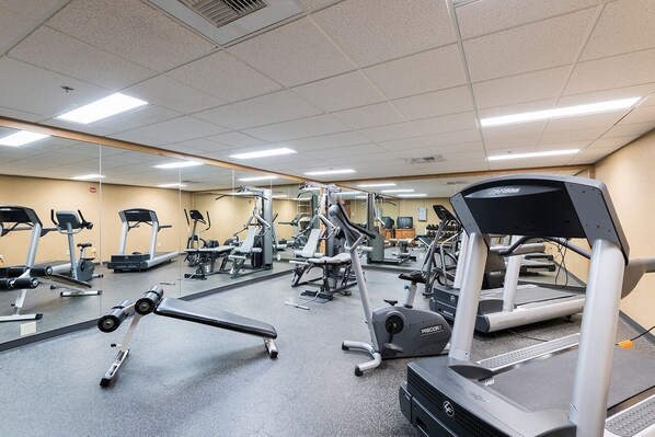 Une salle de sport équipée de divers appareils d’exercice, notamment des tapis de course, des vélos elliptiques et des appareils de musculation.