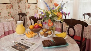 A breakfast table with a newspaper, a fruit bowl, muffins, a loaf of bread, and a vase of flowers. - North Bridge Inn (Concord)