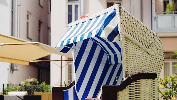 Een rieten lounge stoel met een blauw-witte streep bekleding, een houten basis en een kussen.