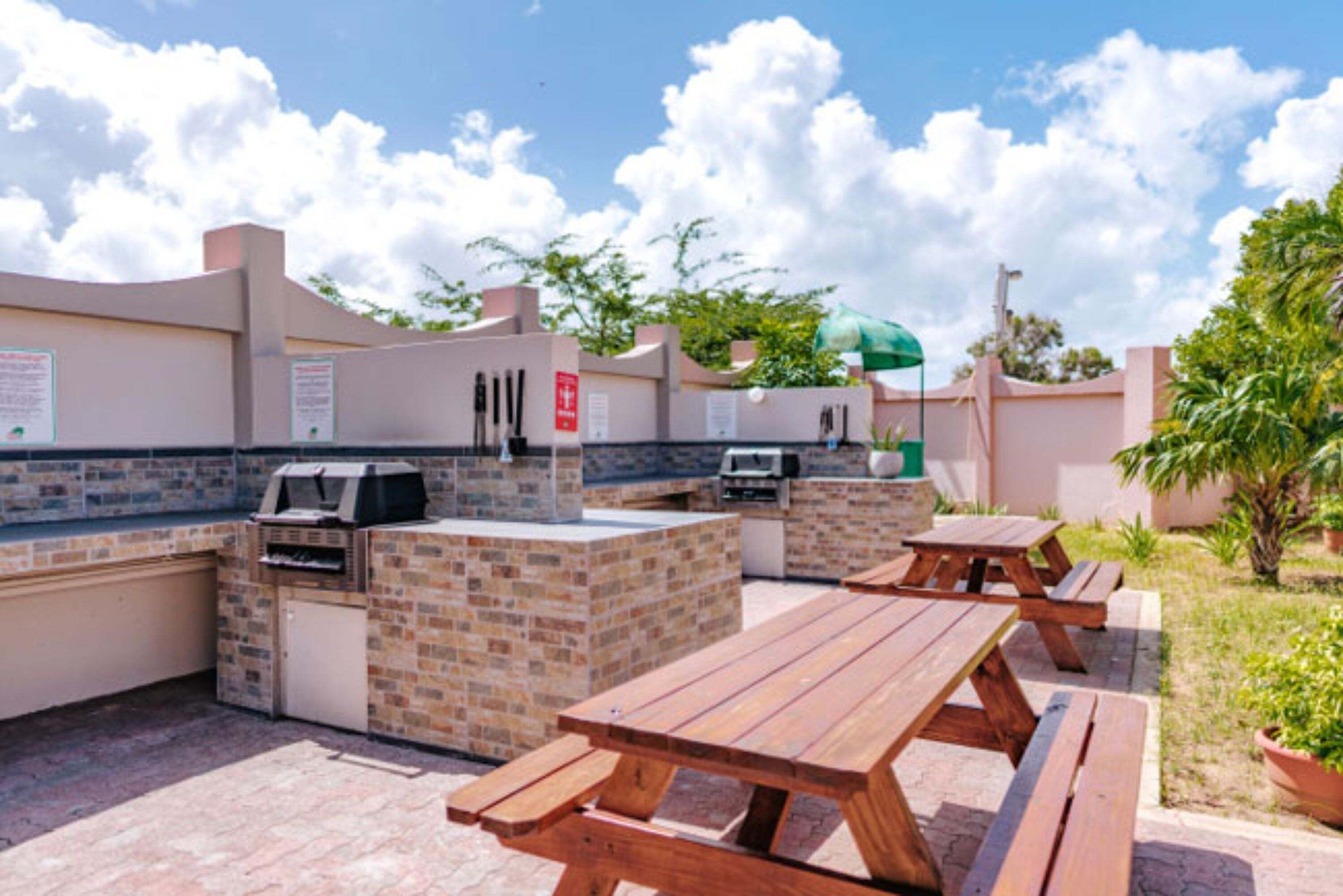 An outdoor patio with a brick barbecue area, picnic tables, and a green umbrella.