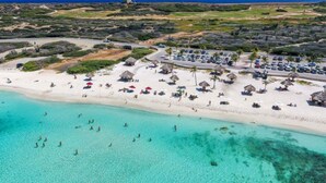 Eine Luftaufnahme eines Strandresorts mit Parkplatz, Strandstühlen und einem klaren türkisblauen Meer.