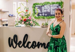 Een receptiegedeelte met een 'Welcome' bord, een menukaart voor koffie en een bloemstuk.