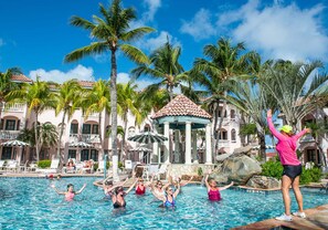 A swimming pool area with palm trees, a gazebo, and a building with a tiled roof. - Caribbean Palm Village Resort (Noord)