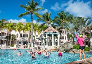 A swimming pool area with palm trees, a gazebo, and a building with a tiled roof.