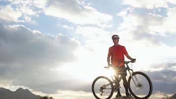 Uma pessoa em pé numa montanha com uma bicicleta, com vista para uma paisagem montanhosa sob um céu nublado.