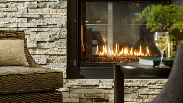 Una chimenea de piedra encendida, un sofá y una silla en una sala de estar.