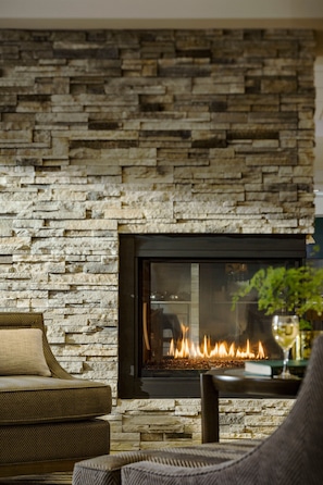 A stone fireplace with a fire, a sofa, and a chair in a living room. - Fairfield Inn & Suites by Marriott Waterbury Stowe (Waterbury)