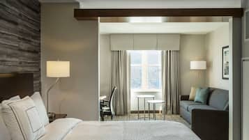 A hotel room with a large bed, a desk with a chair, a sofa, and a window with curtains.