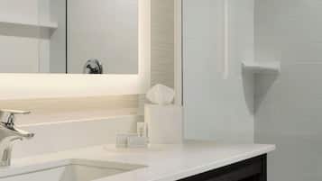 A modern bathroom with a large mirror, a white sink, a dark wooden vanity, and a glass shower enclosure.