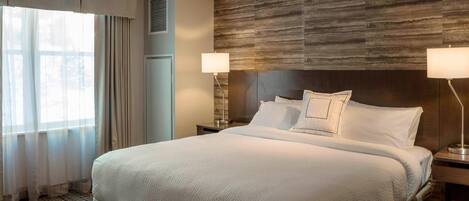 Een hotelkamer met een groot bed, twee bedlampjes, een houten hoofdbord en een raam met gordijnen.