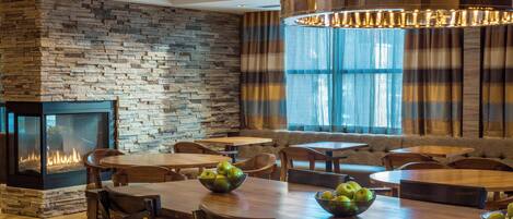 Un restaurant chaleureux avec un mur en pierre, une cheminée et des tables en bois sur lesquelles sont disposés des corbeilles de fruits.