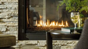 Una chimenea de piedra con frente de vidrio, una mesa de vidrio con un jarrón y un sofá en una sala de estar.