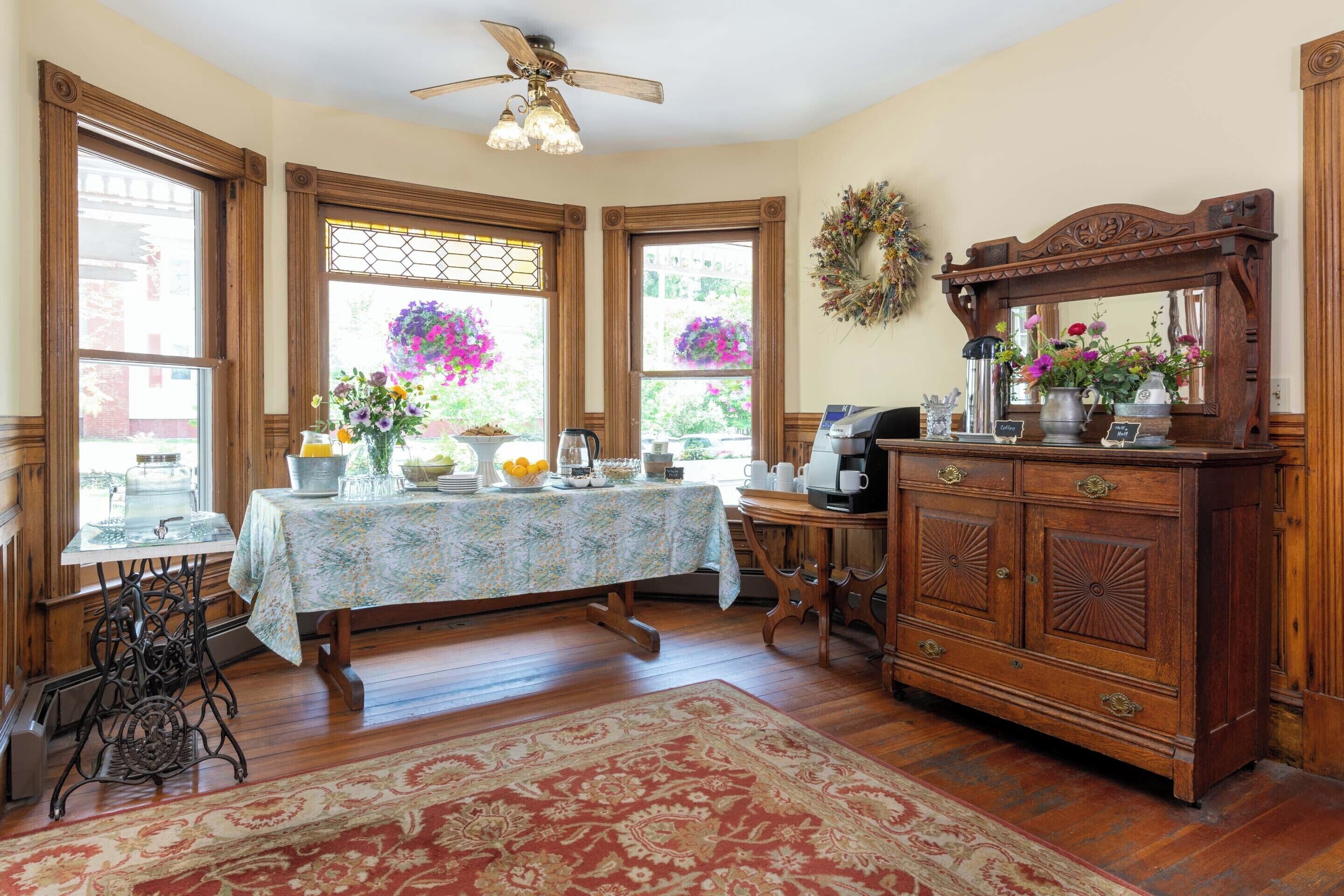 A dining area with a table set for four, a vintage sewing machine, a wooden cabinet, and a ceiling fan.