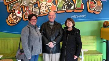 Three people standing in front of a colorful wall with the text "Greetings from Bergery's" and "Vermont".