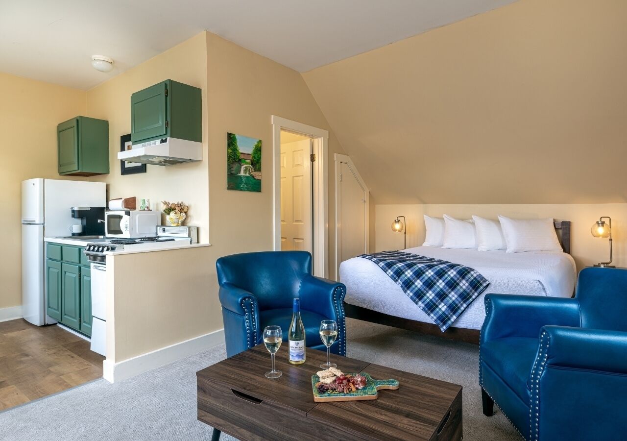 Un espacio habitable compacto con kitchenette, una cama con manta azul y dos sillones azules.