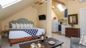 A bedroom with a bed, a breakfast table with cheese and wine, a kitchenette, and a mirror.