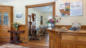 A traditional dining room with wooden furniture, a bulletin board with event information, and a mirror reflecting the room.
