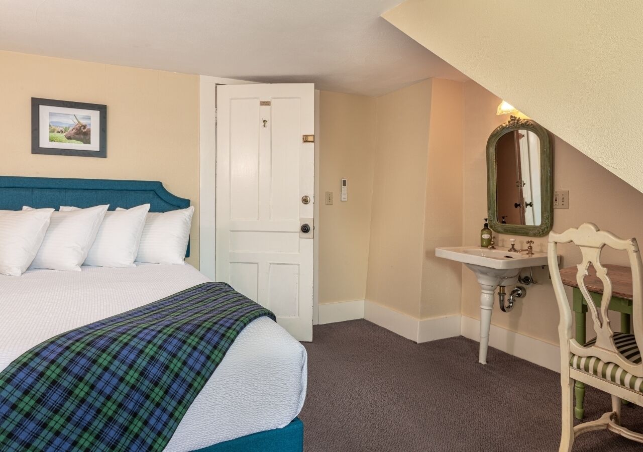 A hotel room with a bed, a white door, a sink, a mirror, and a chair.